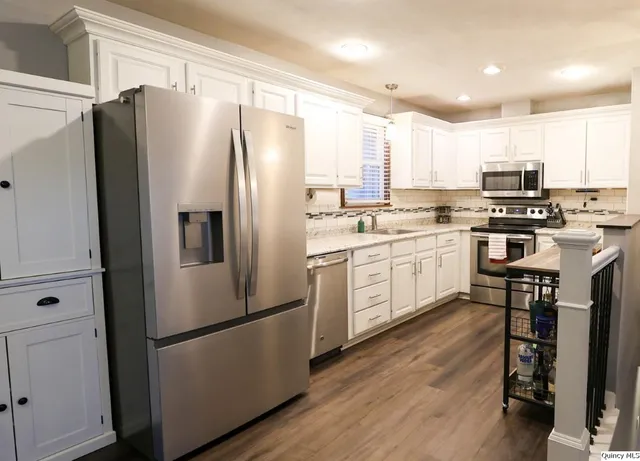 a kitchen with stainless steel appliances a refrigerator a stove a sink and white cabinets