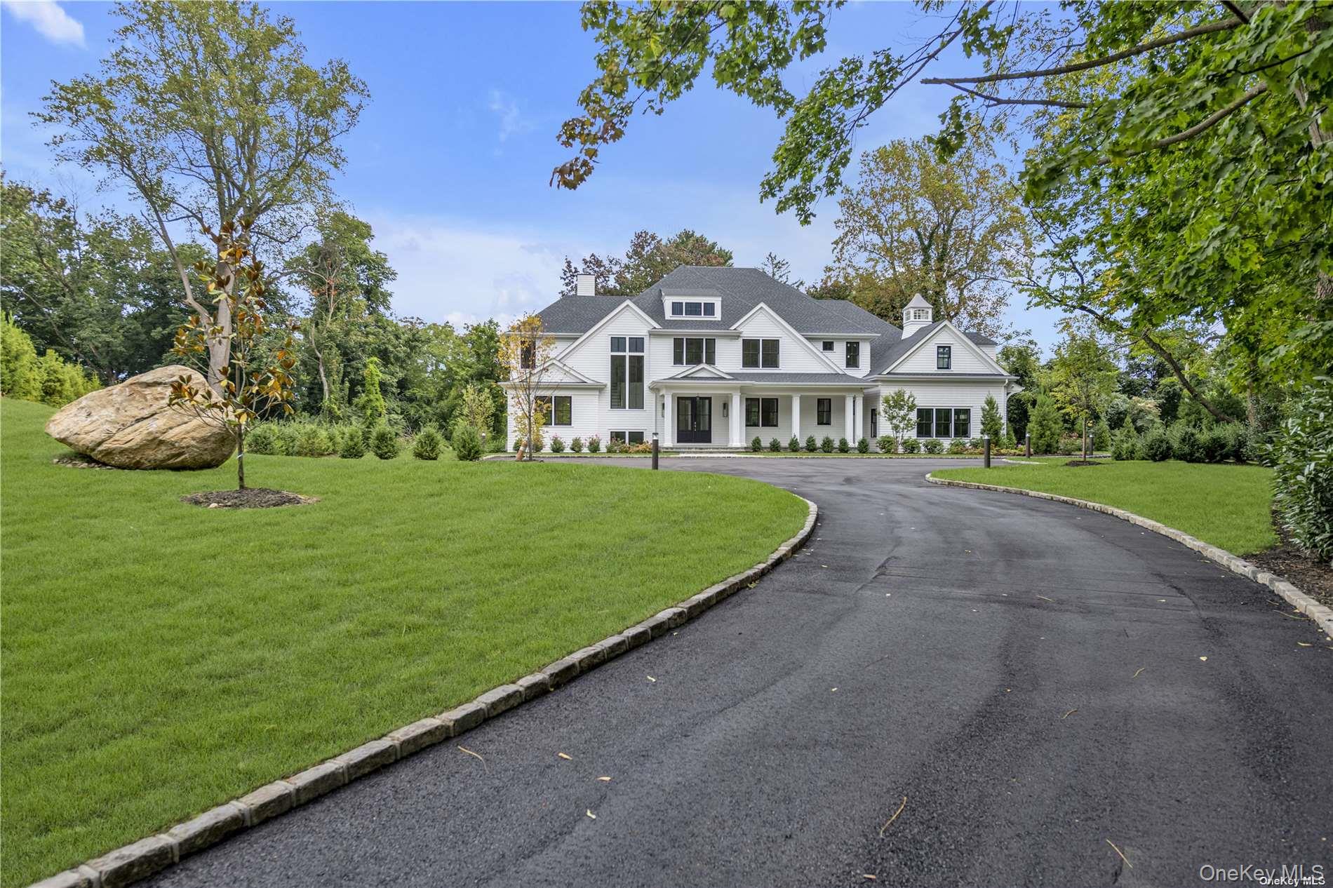 a view of a white house with a big yard plants and large trees