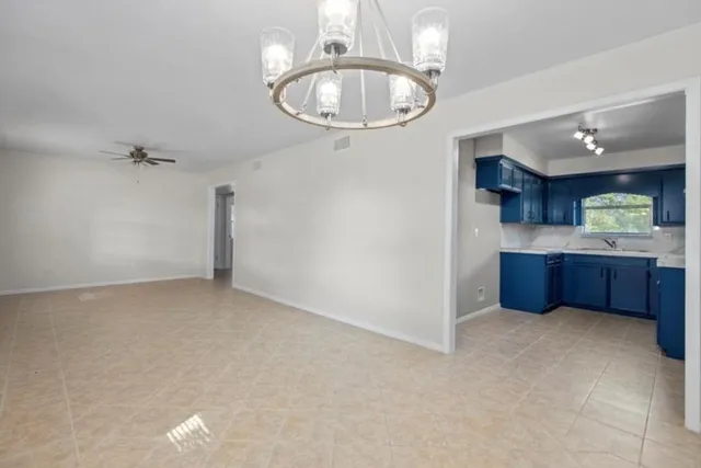 an empty room with kitchen view and a chandelier fan