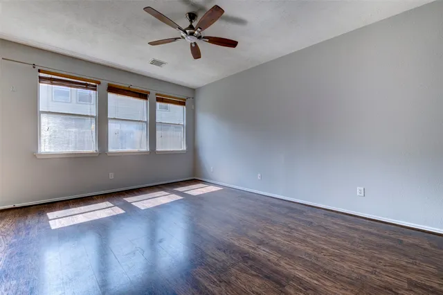 an empty room with wooden floor fan and windows