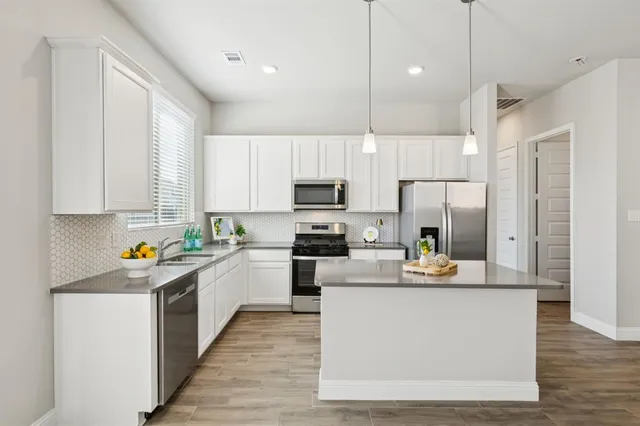 a kitchen with stainless steel appliances a refrigerator a sink a stove a microwave and white cabinets