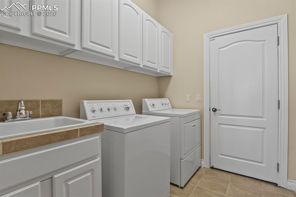 617 Concerto Drive Colorado Springs, CO 80906 - Photo 25 of 46 Laundry room featuring a utility sink with a tiled backsplash, overhead white cabinetry, and tiled flooring