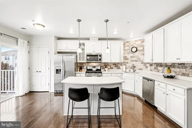 a kitchen with stainless steel appliances kitchen island granite countertop a refrigerator a stove a sink and white cabinets with wooden floor