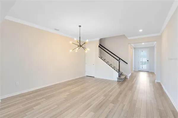 a view of an empty room with wooden floor stairs and a chandelier