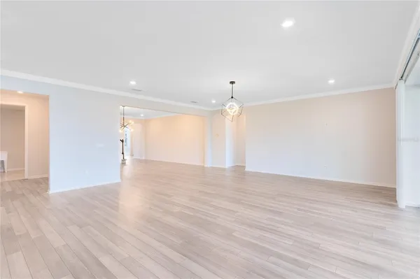 a view of an empty room with wooden floor kitchen view and a window