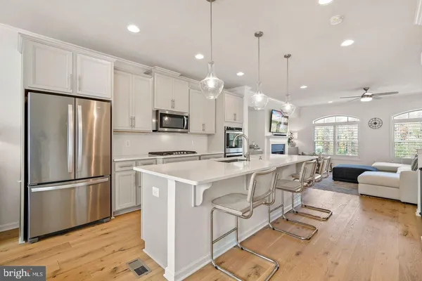 a large white kitchen with a refrigerator a stove a sink and a dining table with wooden floor