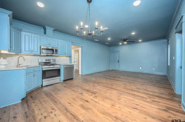 a kitchen with stainless steel appliances granite countertop a sink dishwasher a stove and a refrigerator with wooden floor