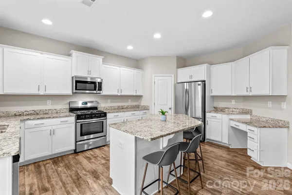 a kitchen with stainless steel appliances granite countertop a stove a sink a microwave a refrigerator and white cabinets