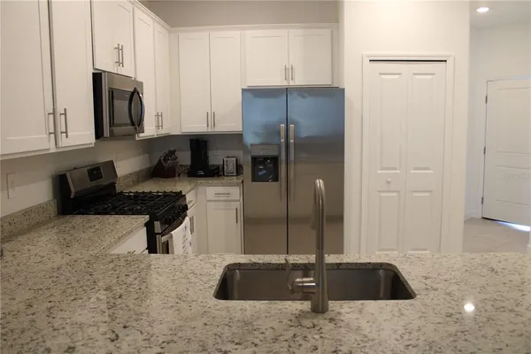 a kitchen with stainless steel appliances granite countertop a refrigerator a stove a sink and white cabinets