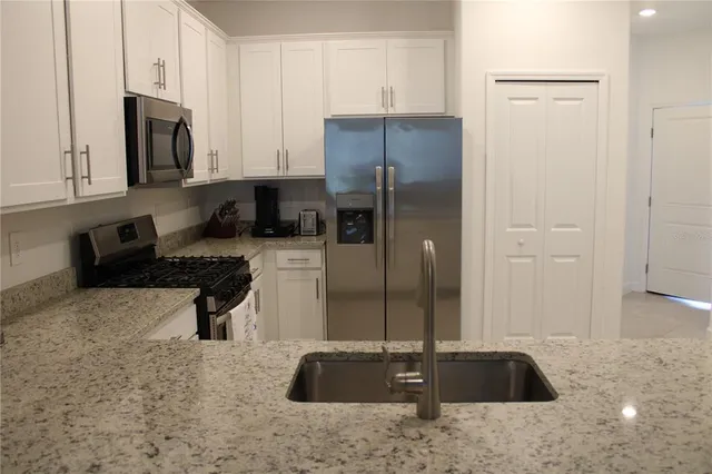 a kitchen with stainless steel appliances granite countertop a refrigerator a stove a sink and white cabinets