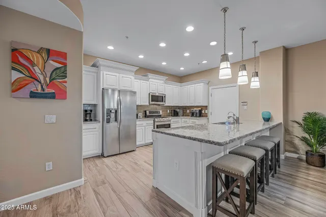 a kitchen with stainless steel appliances granite countertop a refrigerator a oven a sink a dining table and chairs with wooden floor