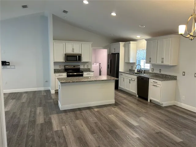 a kitchen with stainless steel appliances granite countertop a stove top oven a sink and white cabinets with wooden floor