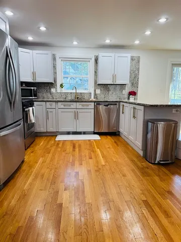 a kitchen with stainless steel appliances granite countertop a stove top oven a refrigerator a sink and white cabinets