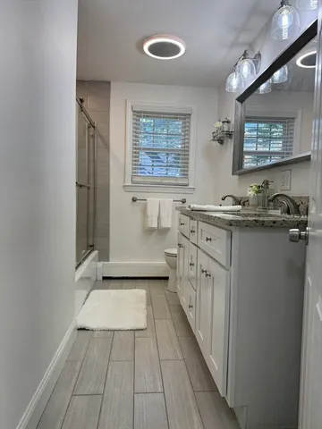 a bathroom with a granite countertop sink a toilet a mirror and shower