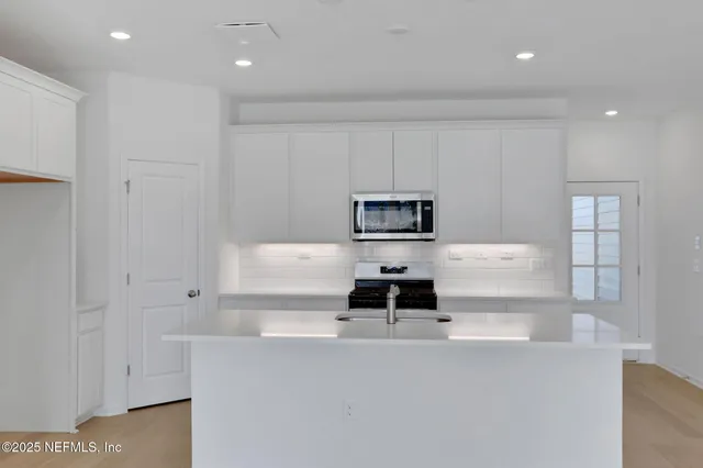 a kitchen with stainless steel appliances a refrigerator a stove and white cabinets
