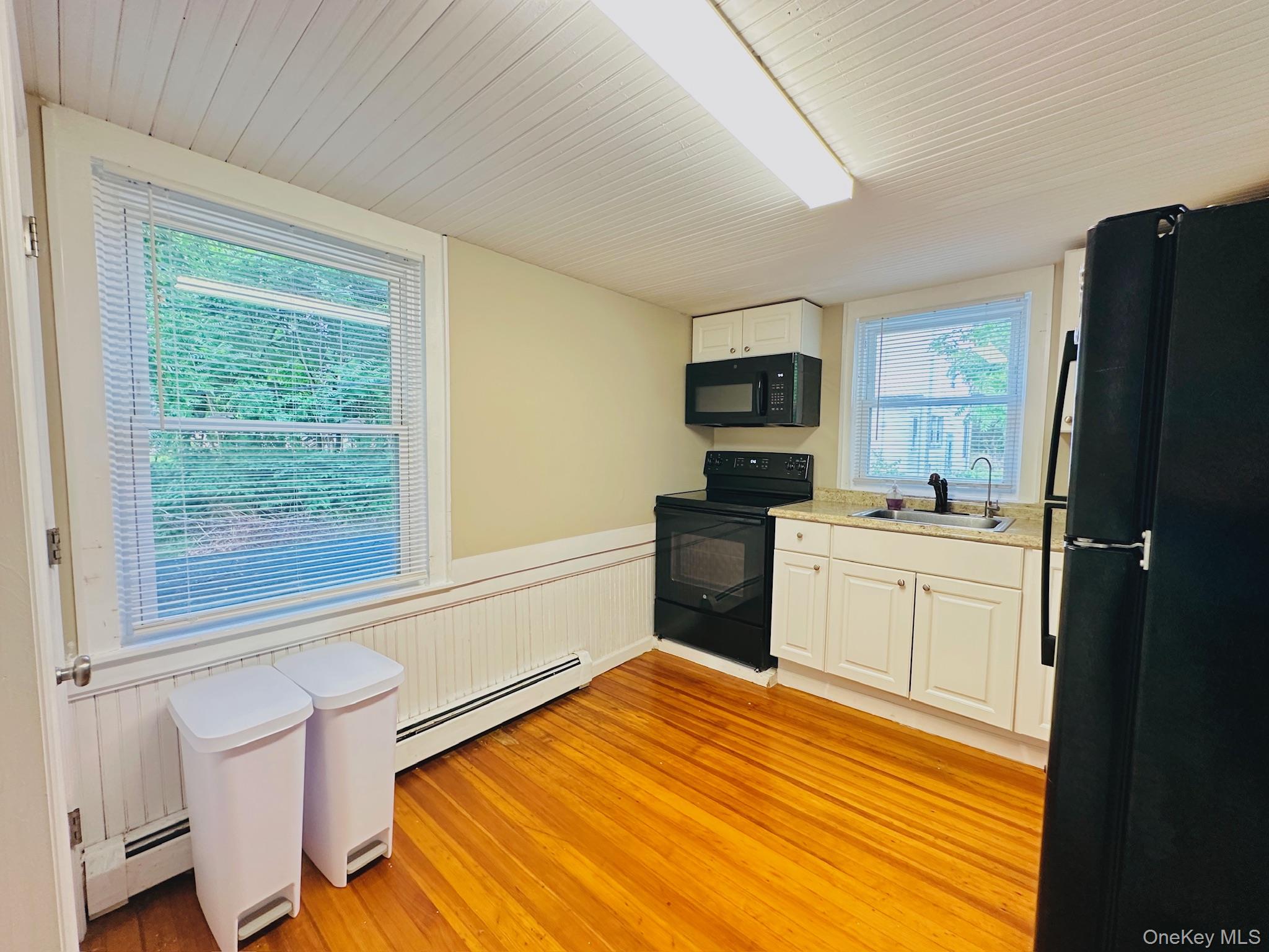 181 Mansion Street, Unit 2 Poughkeepsie, NY 12601 - Photo 4 of 20 Kitchen featuring black appliances, a baseboard heating unit, white cabinets, light wood finished floors, and wainscoting