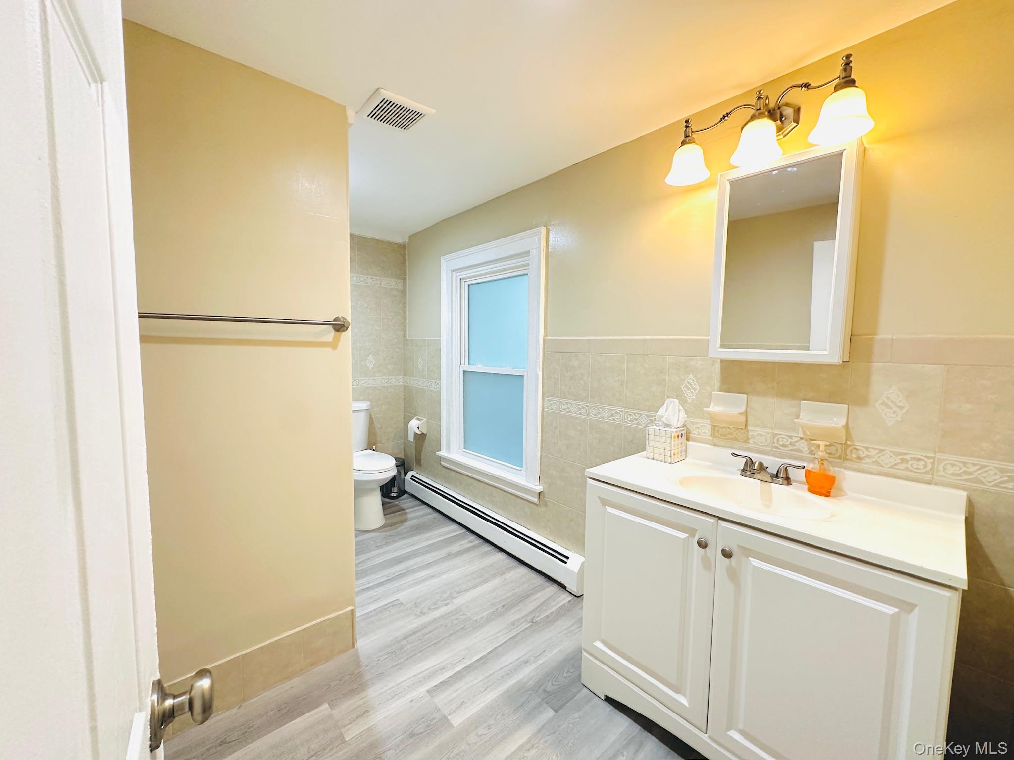 181 Mansion Street, Unit 2 Poughkeepsie, NY 12601 - Photo 7 of 20 Bathroom featuring a baseboard heating unit, vanity, tile walls, light wood-style flooring, and a wainscoted wall