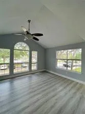 an empty room with wooden floor fan and windows