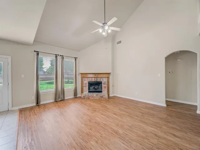 an empty room with wooden floor fireplace and windows