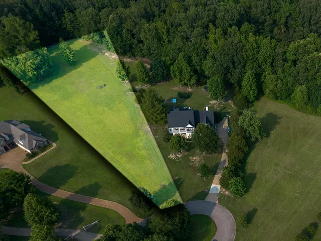 an aerial view of a residential houses with outdoor space and trees all around