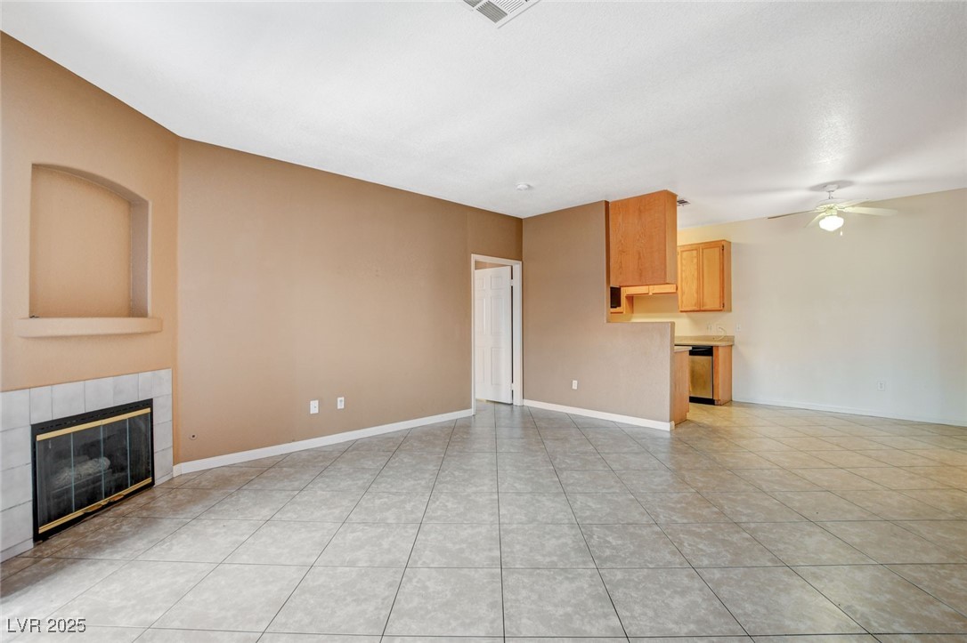 Unfurnished living room featuring a tiled fireplace, ceiling fan, and light tile patterned floors