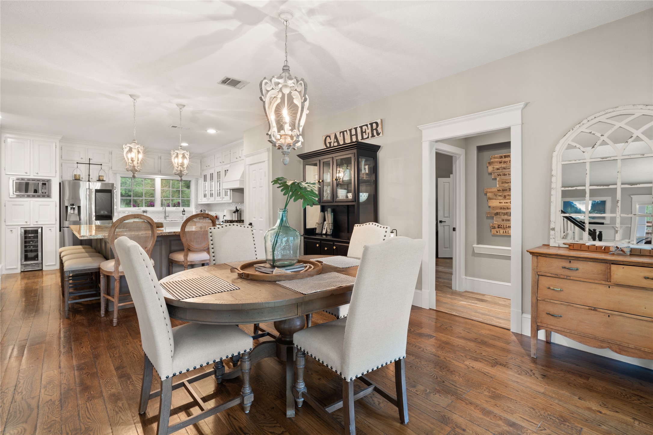 36 Wind River Drive Conroe, TX 77384 - Photo 25 of 45 This photo showcases a warm, inviting open-concept kitchen and dining area. It features hardwood floors, a stylish round dining table with upholstered chairs, and elegant pendant lighting above a spacious kitchen island. The kitchen has modern appliances, white cabinetry, and a cozy ambiance perfect for gatherings.