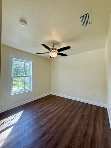 an empty room with wooden floor fan and windows
