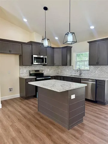 a kitchen with stainless steel appliances granite countertop a sink a stove a refrigerator and a wooden floor