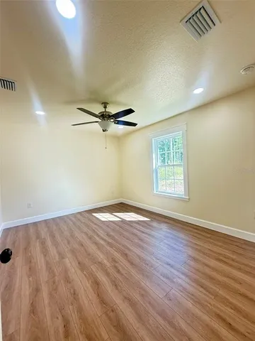an empty room with wooden floor fan and windows