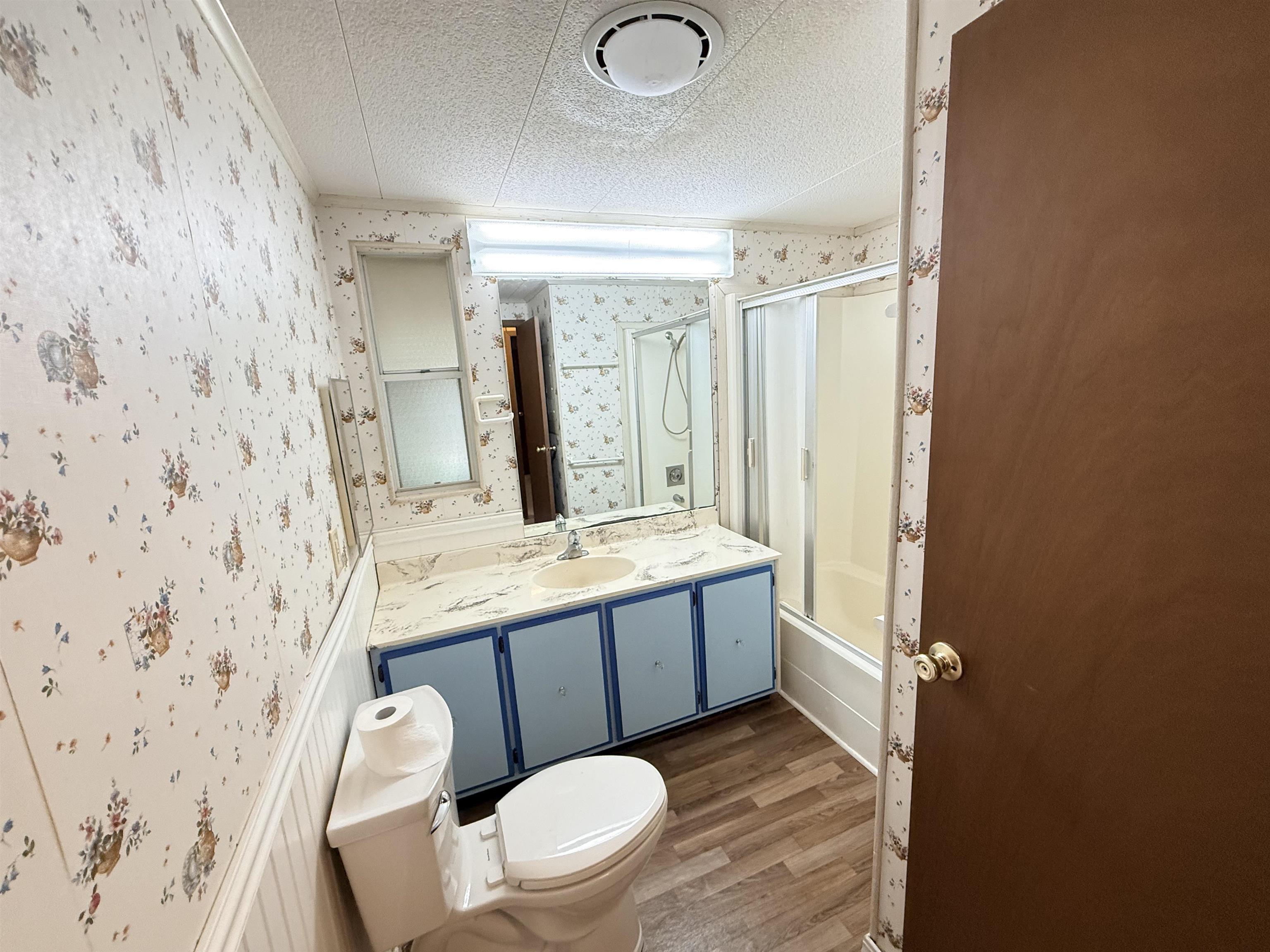 3043 Atlanta Circle Murrells Inlet, SC 29576 - Photo 17 of 36 Bathroom featuring vanity, wallpapered walls, light wood-style floors, bath / shower combo with glass door, and a textured ceiling