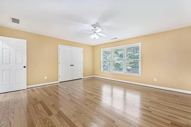 an empty room with wooden floor chandelier fan and windows