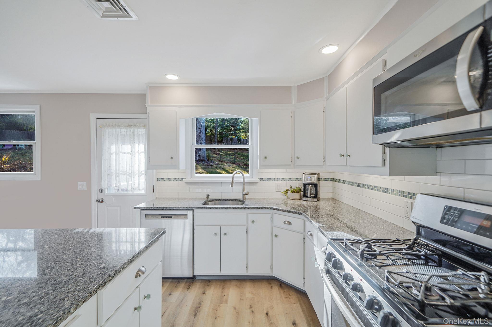 12 Harbor Beach Road Miller Place, NY 11764 - Photo 11 of 45 Kitchen featuring appliances with stainless steel finishes, white cabinets, light wood finished floors, light stone countertops, and ornamental molding