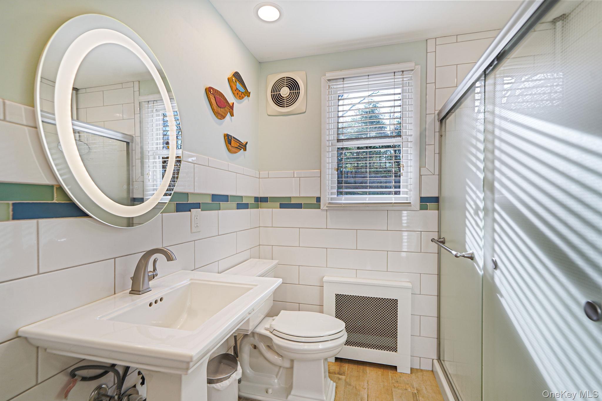 12 Harbor Beach Road Miller Place, NY 11764 - Photo 14 of 45 Full bath featuring a shower stall, tile walls, radiator, light wood-type flooring, and wainscoting