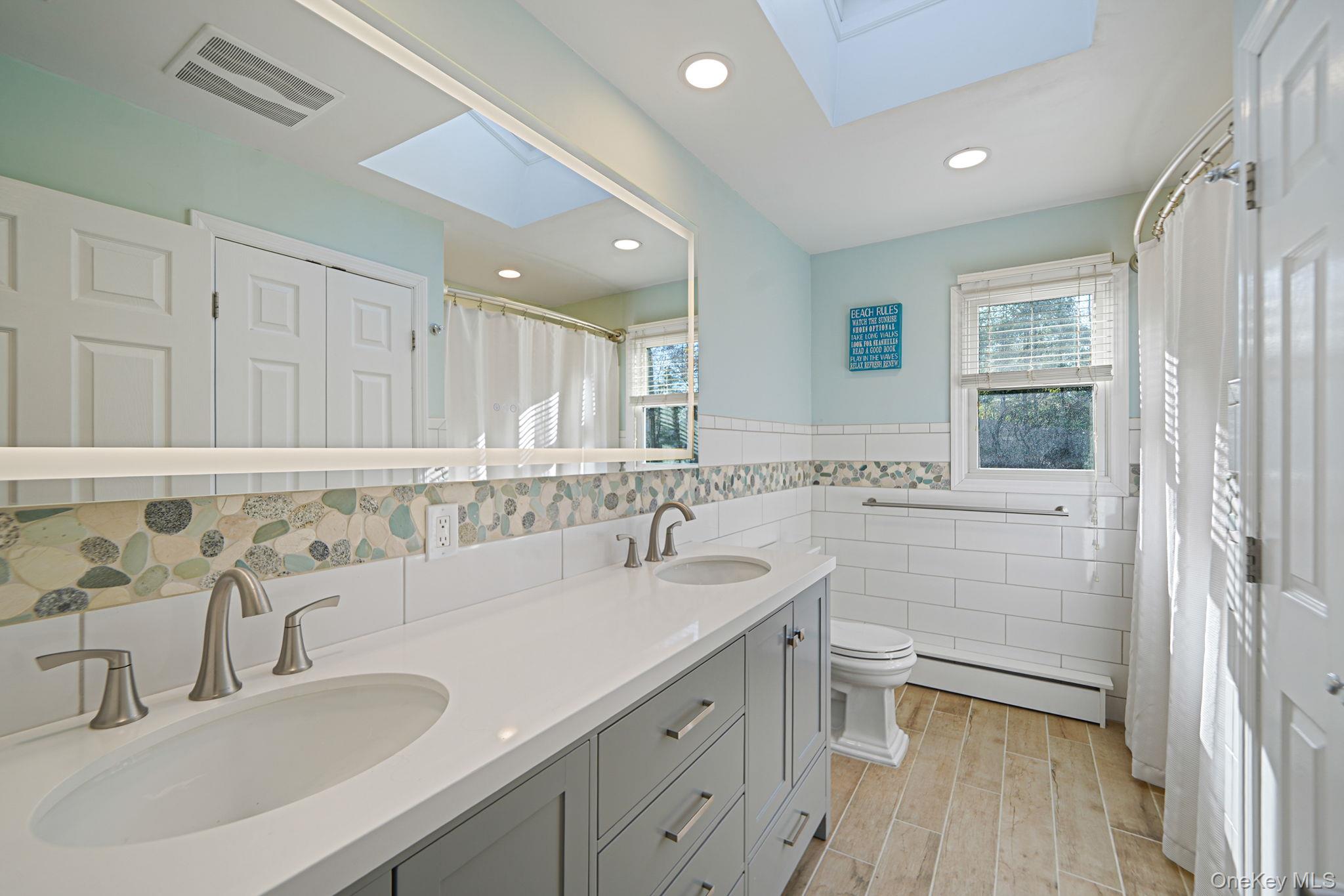 12 Harbor Beach Road Miller Place, NY 11764 - Photo 30 of 45 Full bathroom featuring a skylight, a shower with curtain, double vanity, a baseboard radiator, and tile walls