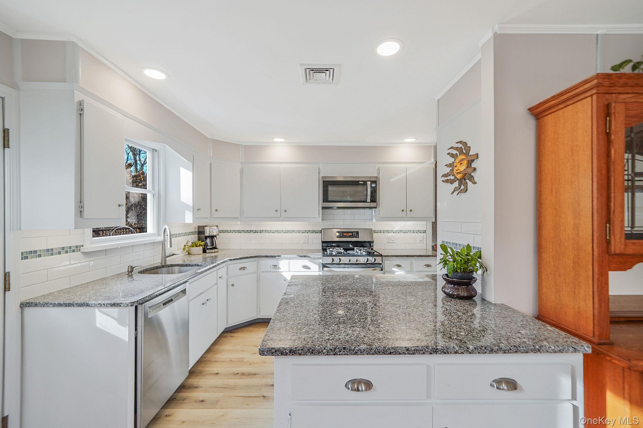 12 Harbor Beach Road Miller Place, NY 11764 - Photo 8 of 45 Kitchen featuring dark stone countertops, light wood finished floors, appliances with stainless steel finishes, white cabinets, and backsplash