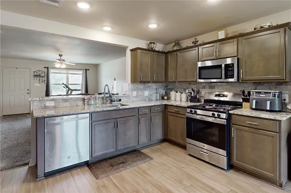 a kitchen with stainless steel appliances granite countertop wooden cabinets a sink a stove a microwave and wooden floors