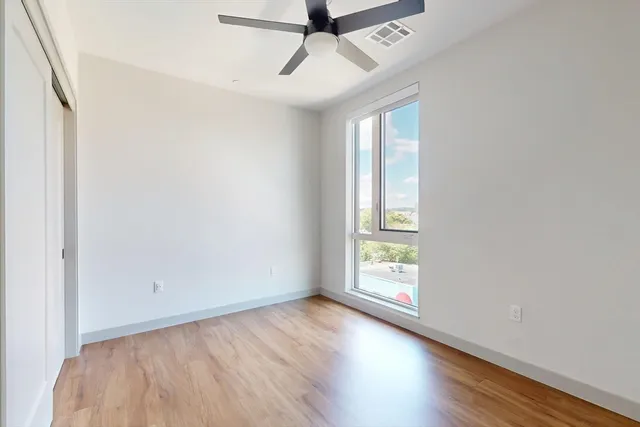 an empty room with wooden floor chandelier fan and windows