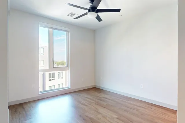 an empty room with wooden floor fan and windows