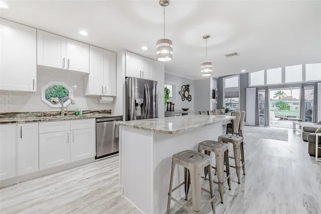 a kitchen with stainless steel appliances kitchen island granite countertop a dining table chairs refrigerator sink and cabinets