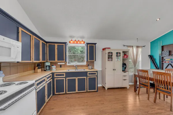 a kitchen with stainless steel appliances a sink a stove a refrigerator cabinets and a dining table with wooden floor