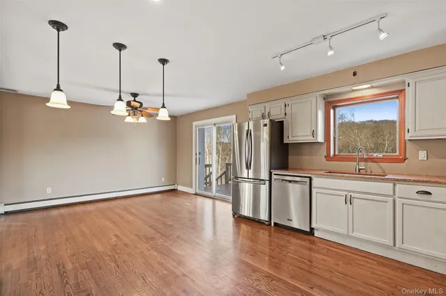 a view of a kitchen with stainless steel appliances granite countertop a sink a microwave oven a refrigerator and white cabinets with wooden floor