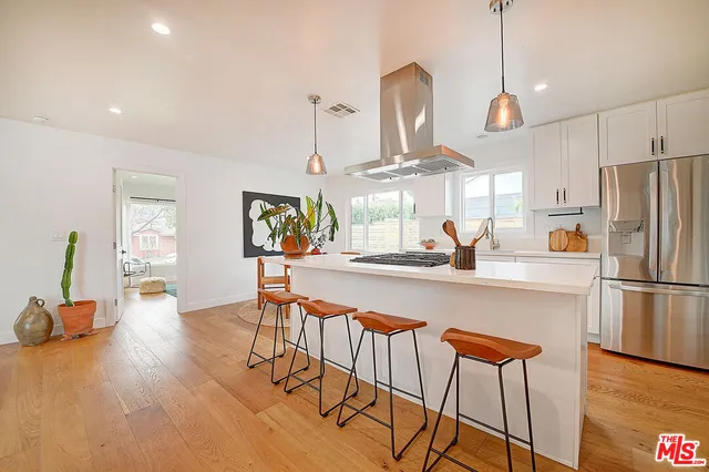 a kitchen with stainless steel appliances granite countertop a refrigerator a sink dishwasher a dining table and chairs with wooden floor