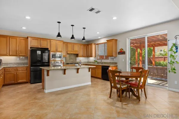 a kitchen with stainless steel appliances granite countertop a stove top oven a sink dishwasher a dining table and chairs with wooden floor