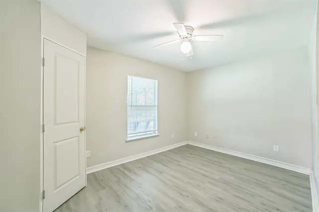an empty room with wooden floor fan and windows