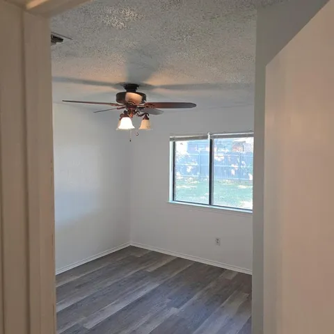 an empty room with wooden floor fan and windows