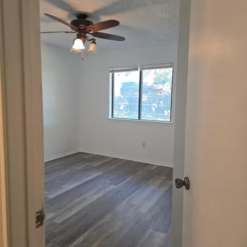 an empty room with wooden floor fan and windows