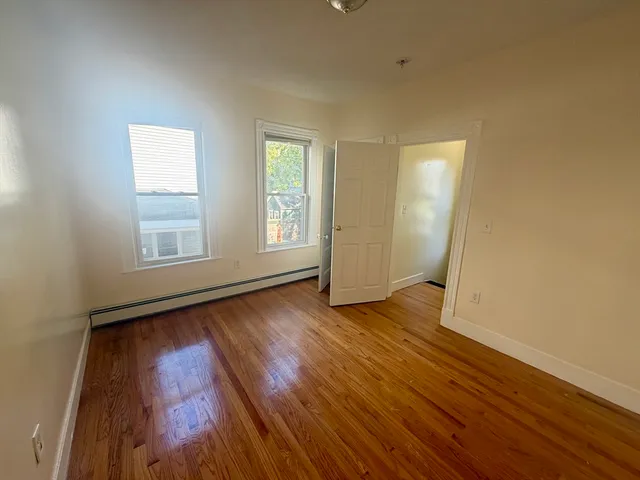 a view of an empty room with wooden floor and window