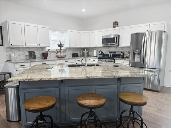 a kitchen with stainless steel appliances granite countertop a table chairs stove refrigerator and cabinets