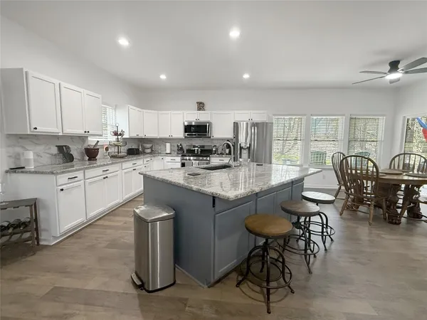 a kitchen with stainless steel appliances granite countertop a table chairs sink and cabinets