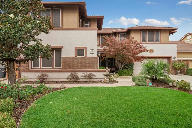 a front view of a house with garden and a tree